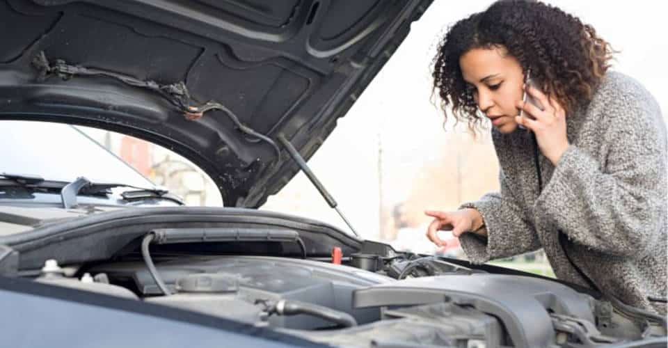 woman on phone opens car hood to look at engine